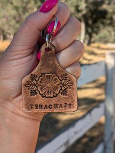 a hand holding a leather keychain that says terrachat on it and has a flower design