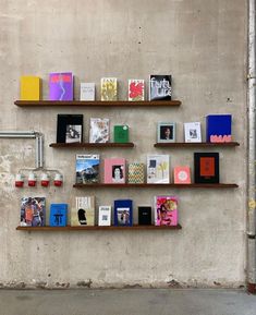 several books are arranged on wooden shelves against a concrete wall, with a pipe in the background