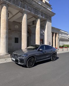 a grey bmw suv parked in front of a large building with columns on the side