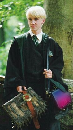 a young man dressed in harry potter robes holding a book and bag with both hands