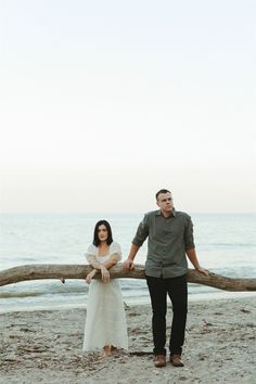 a man and woman standing next to each other on top of a sandy beach near the ocean