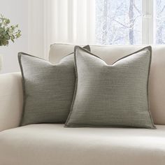 two pillows sitting on top of a couch next to a vase with flowers in it