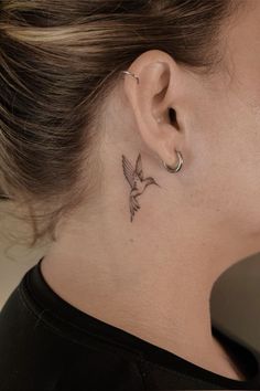 a woman's neck with a small bird tattoo on her left side behind the ear