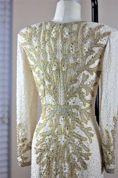 the back of a white dress with gold and silver beading