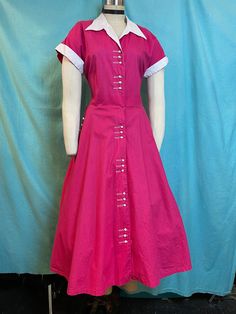 "1950s W:32 Dark Pink Magenta cotton fit and flare white pique collared short sleeve button up dress with pockets! Vintage 50s beautiful fit and flare dress. Made out of solid dark pink/magenta cotton with cotton pique white contrast. Bodice darted, with cuffed sleeves and collared neckline. Rows of 3 plastic buttons that looks like a small toothpaste caps. One of a kind. Unlined. Added petticoat not included.  MEASUREMENTS  Bust: 40\" Waist: 32\" Hips: free Bodice length: 18\" Skirt length: 30\" with no hem available to let down This is in good vintage condition, overall wear to fabrics due age, presents beautifully and is completely wearable as is! ✨" Classic Short Sleeve Dress With Button Cuffs, Fitted Cotton Shirt Dress With Placket, Fitted Vintage Dress With Short Sleeves, Classic Short Sleeve Dresses With Covered Buttons, Classic Short Sleeve Shirt Dress With Buttons, 1950s Style Short Sleeve Day Dresses, 1950s Style Vintage Dress With Short Sleeves For Daywear, 1950s Style Short Sleeve Dresses For Daywear, Retro Fitted Shirt Dress With Buttons