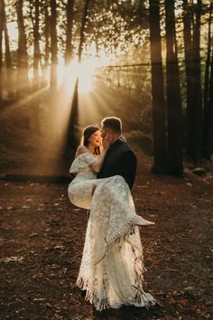 a bride and groom are hugging in the woods at their wedding day with sun shining through the trees