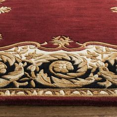 a red rug with gold and black designs on the bottom, sitting on a wooden floor