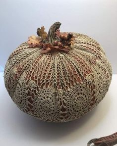 a decorative pumpkin with crochet and leaves on it sitting next to a pair of scissors