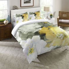 a white bed with yellow and green flowers on it next to a window in a room