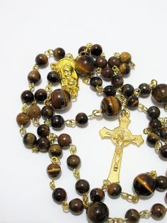 "This Tiger's eye Catholic rosary is made with Grade a gemstones. The hand turned links are gold plated as is the connector. The golden cross is from Italy. The rosary measures 26\" in the body and has a 5\" cross drop. This rosary will be slipped into a velvet bag and shipped in a bubble mailer." Gold Rosary With Gemstone Beads Gift, Gold Rosary Bracelet With Cross And 8mm Beads, Gold Spiritual Rosary With Gemstone Beads, Gold Spiritual Rosary Bracelet With Polished Beads, Gold Rosary Bracelet With Natural Stones And Round Beads, Gold Gemstone Beads Rosary, Spiritual Gold Rosary With 8mm Beads, Gold Spiritual Rosary With Round Beads, Gold Spiritual Rosary With Cross