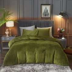 a bed with green comforter and pillows in a room next to a lamp on a table