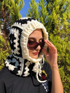 a woman wearing sunglasses and a crocheted hat on top of her head with trees in the background