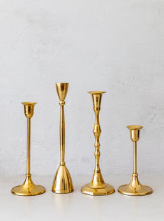 three gold candlesticks are lined up on a white surface, with one candle in the middle