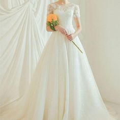 a woman in a white wedding dress holding a yellow rose and looking at the camera