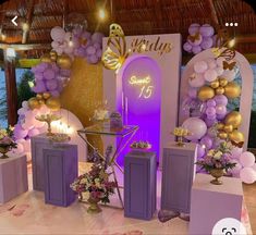 a stage set up for a party with purple and gold decorations on the walls, candles and balloons