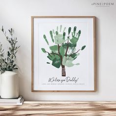 a framed print of a handprint tree on a shelf next to a potted plant