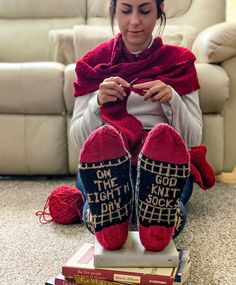 a woman is sitting on the floor with her feet up and knitting in slippers