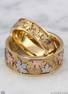 two gold wedding rings with maple leaves on them sitting next to each other in front of a marble background