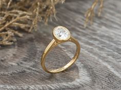 a yellow gold ring with a single diamond on the top, sitting next to some branches