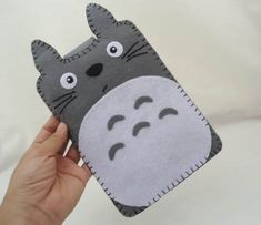 a hand holding up a small totoro pillow with eyes and nose drawn on it