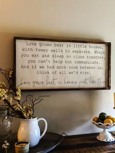 a wooden sign hanging on the wall above a table with flowers and fruit in vases