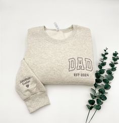 a white sweatshirt with the word dad printed on it next to some green leaves and a plant