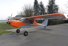 an orange and white plane is parked on the pavement in front of some houses with trees