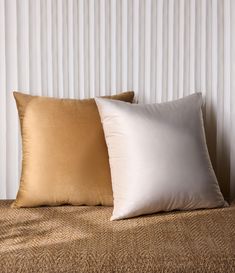 two pillows sitting on top of a bed next to a white and gold striped wall