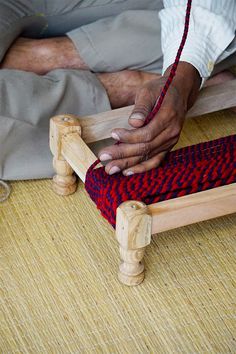 a person weaving on a wooden frame with red and blue material in the background,