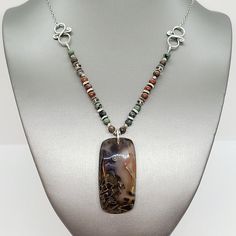 Made with love, this necklace features a stunning Stick Agate pendant stone flanked by Bronzite, Biotite, Mahogany Jasper, Smokey Quartz, and Hill Tribe Silver. At 22 3/4" long, this piece is sure to make a statement! Check out the coordinating earrings. Nickel-free Jasper Jewelry As A Gift, Nickel-free Jasper Jewelry For Gifts, Earthy Ocean Jasper Jewelry With Natural Stones, Earthy Ocean Jasper Jewelry Gift, Sterling Silver Brown Wire Wrapped Jewelry, Unique Nickel-free Agate Jewelry, Brown Jasper Gemstone Jewelry, Handmade Earthy Sterling Silver Jewelry, Earthy Sterling Silver Jewelry With Natural Stones