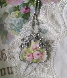 a close up of a necklace on a lace doily with flowers in the background