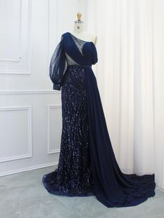 Step into elegance with our Navy Blue One-Shoulder Sequin Gown, a stunning masterpiece for any formal occasion. This sophisticated dress features an asymmetrical one-shoulder design, complemented by a translucent, long chiffon sleeve, adding an element of drama and grace. The bodice is beautifully draped, creating a flattering silhouette that will make you feel like a true diva.The gown is adorned with intricate sequins that shimmer with every movement, ensuring all eyes are on you. The rich navy blue color exudes timeless sophistication, making it a perfect choice for evening events, galas, and weddings. A sweeping train adds a touch of luxury, transforming your entrance into an unforgettable moment.Crafted with the highest quality materials, this gown ensures comfort without compromising One Shoulder Evening Dress With Sweep Train For Prom, One-shoulder Evening Dress With Sweep Train For Prom, Gala Gown With Sweep Train And One Shoulder, One Shoulder Gown With Sweep Train For Gala, One-shoulder Gown With Sweep Train For Gala, Off-shoulder Evening Dress With Detachable Train, Floor-length Evening Dress With Sheer Sleeves For Banquet, Blue One Shoulder Dress For Prom, Sheer Sleeves Floor-length Evening Dress For Banquet