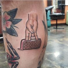 a tattoo on the leg of a man with a hand holding a suitcase and flowers