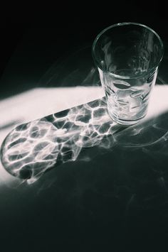 a glass sitting on top of a table next to a light reflecting off the floor