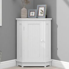 a white cabinet with two pictures on top and a vase next to it in the corner