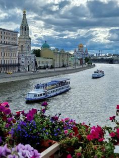 two boats are traveling down the river in front of some old buildings and colorful flowers