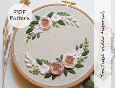 an embroidered hoop with pink flowers and green leaves on it, next to some scissors