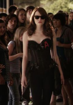 a woman with sunglasses on is walking in front of a group of people wearing black clothing