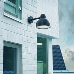 a black lamp on the side of a white brick building next to a potted plant