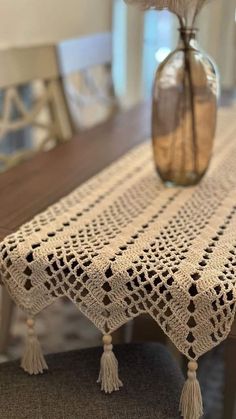 a crocheted table runner with tassels on it and a vase filled with flowers