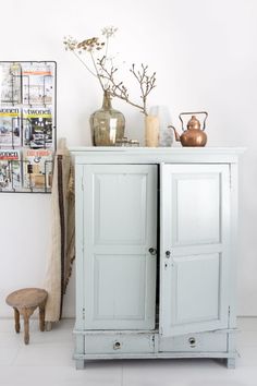 a white cabinet sitting next to a wall with vases and other items on it