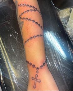 a woman's arm with a rosary tattoo on it and a cross in the middle