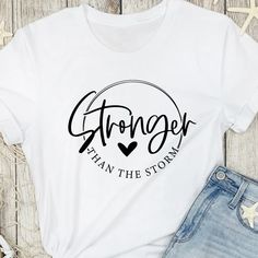 Empower yourself or a loved one with our 'Stronger than the Storm' Inspirational Script T-Shirt, a symbol of strength and determination during life's challenges. This stylish tee features the uplifting quote "Stronger than the Storm" elegantly rendered in a beautiful script font, accompanied by a heart motif. It's the perfect gift for those facing adversity or anyone in need of a reminder that they can overcome any storm that life presents. T Shirt Quotes Women, Fun Shirts Sayings, Inspirational T Shirts For Women, Inspirational Shirts Women, Quotes For T Shirts Design, Inspirational Tshirts Ideas, Cute Tshirts Women, T Shirt Ideas Sayings, Custom Tshirt Ideas