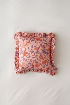 an orange and pink floral pillow with ruffled edges on a white bedding sheet