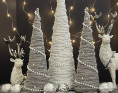 three white christmas trees decorated with lights and reindeer figurines next to each other