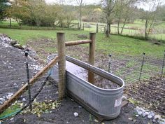 an empty tub sitting in the middle of a field next to a fence and grass