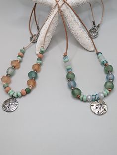 "Summer jewelry! These handmade ocean beach vibe beaded pendant necklaces feature a silver sand dollar pendant, recycled African glass beads in blue green and peach colors, faceted crystal beads, other handmade glass beads and silver beads strung on 1mm leather cord with a silver toggle clasp.  The length is 21.5\" including pendant. The leather color on the peach/green necklace is Petal/cream The leather color on the green/blue necklace is Natural/tan. They are very lightweight and fun to wear, I always get comments when I have mine on! These are made to order so there may be some slight variations in the size and shades of the recycled glass. All jewelry comes in a gift box or a drawstring gift bag Thanks for stopping by my Etsy shop, hope you found something you love!" Recycled Glass Bead Necklace, Recycled Glass Bead Jewelry, Beachy Necklaces, Chest Jewelry, Beachy Necklace, Glass Bead Jewelry, Sand Dollar Pendant, Boho Necklaces, Drawstring Gift Bag