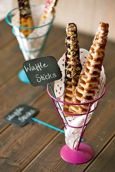 three waffle sticks are sitting in small glass vases on a table with a chalkboard sign