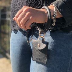 This faux leather bangle is perfect for bringing with you on the go! You can hang your keys, Cuticle Buddy® and/or our new portable glass nail files off of it. The button closure wallet can store credit cards or money. Wear as a bracelet or hold like a purse! Features gold toned metal details and a tassel addition. Vegan. Made from 100% polyurethane leather. Cuticle Buddy® not included. Black Wristlet With Cell Phone Pocket For Gift, Black Wristlet With Cell Phone Pocket As Gift, Adjustable Wristlet With Interior Key Chain Holder For Travel, Black Keychains With Interior Key Chain Holder, Versatile Wallet With Interior Key Chain Holder As Gift, Daily Use Wristlet With Key Leash, Rectangular Wristlet With Key Clip For Everyday, Everyday Use Rectangular Wristlet With Key Clip, Everyday Rectangular Wristlet With Key Clip