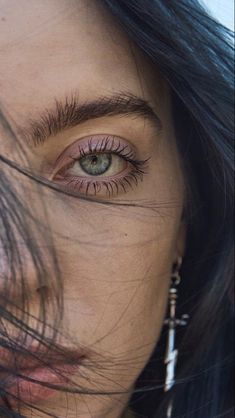 a woman's eye with long black hair and piercings on her nose, looking at the camera